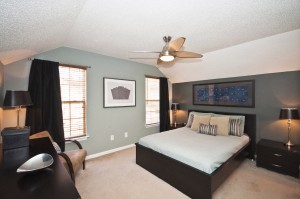 Bedroom with blue and gray walls white popcorn ceiling with ceiling fan carpet flooring two windows with black curtains