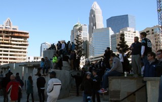 Crowd of people in uptown Charlotte outside Bank of America stadium with skyline behind them