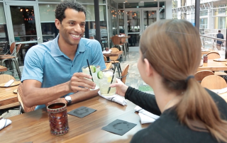 Matthew Means and a women clinking their drinks sitting in an outdoor seating area of a restaurant