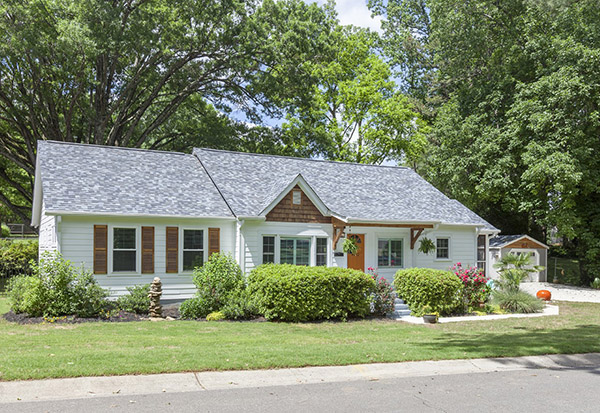 Home with white siding and wooden brown shutters and wooden shingle details orange front door tree filled backyard