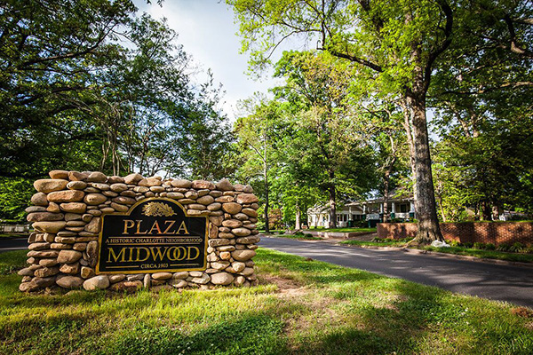 Stone Plaza Midwood sign in the middle of grass on the side of tree lined street