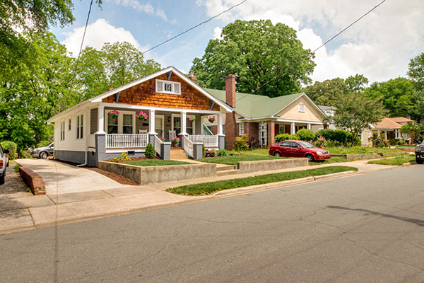 Gray and white siding home with brown shingles on front of the roof front porch with white columns and railing sidewalk and street in front